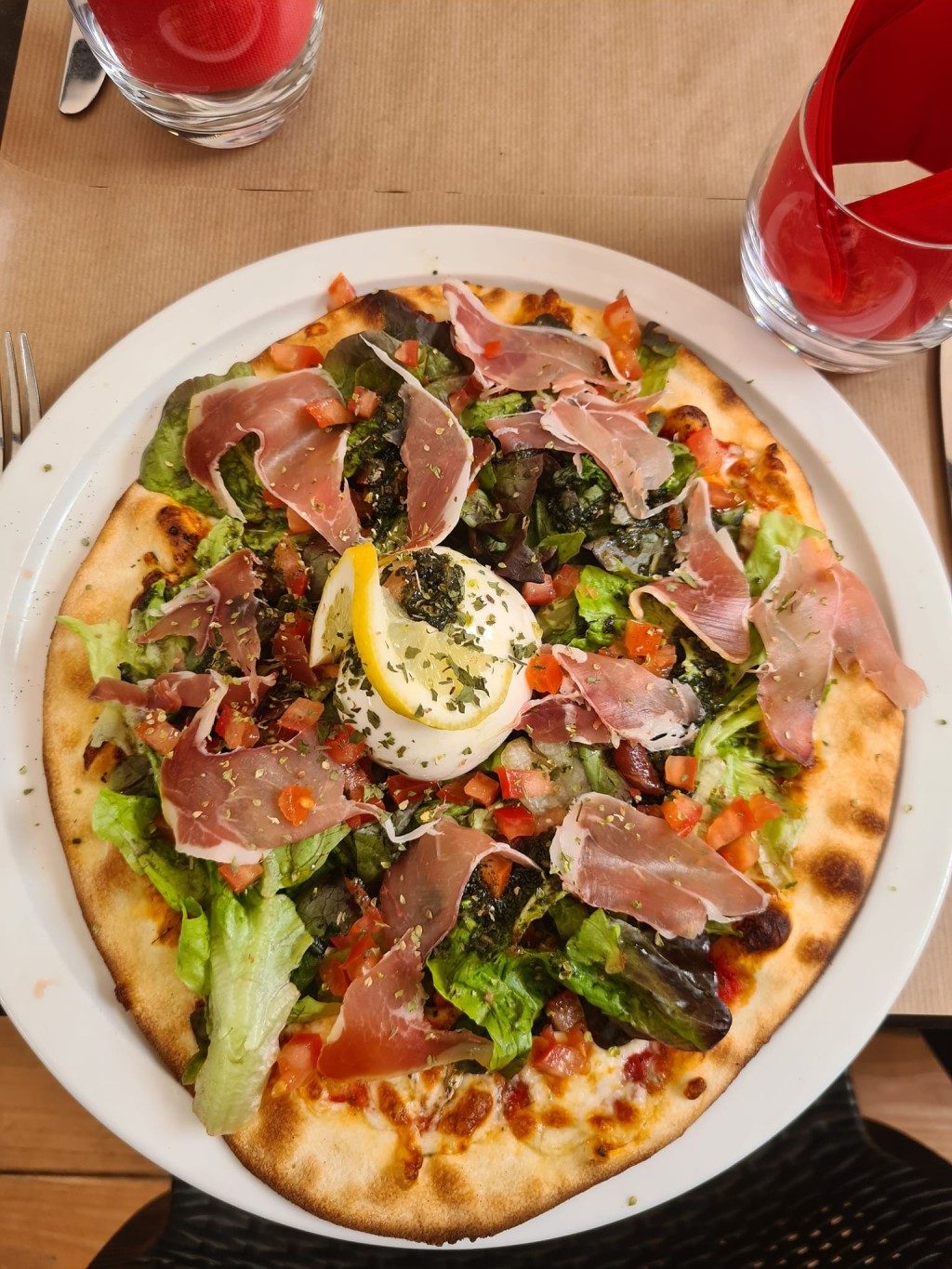 Une pizza fine au jambon cru, roquette et burrata, sur une assiette blanche