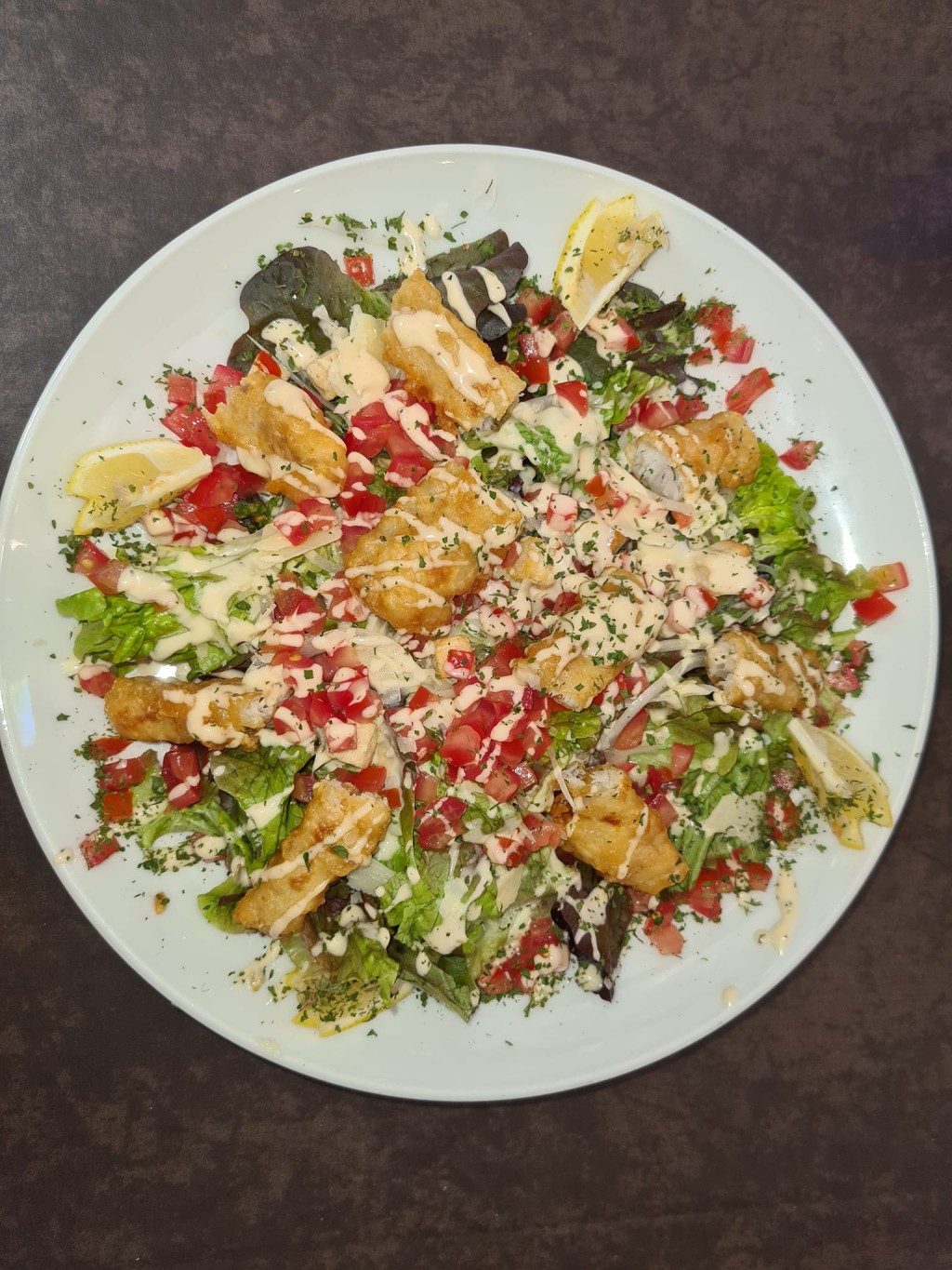 Une grande salade composée avec du poulet croustillant, des tomates et une sauce crémeuse