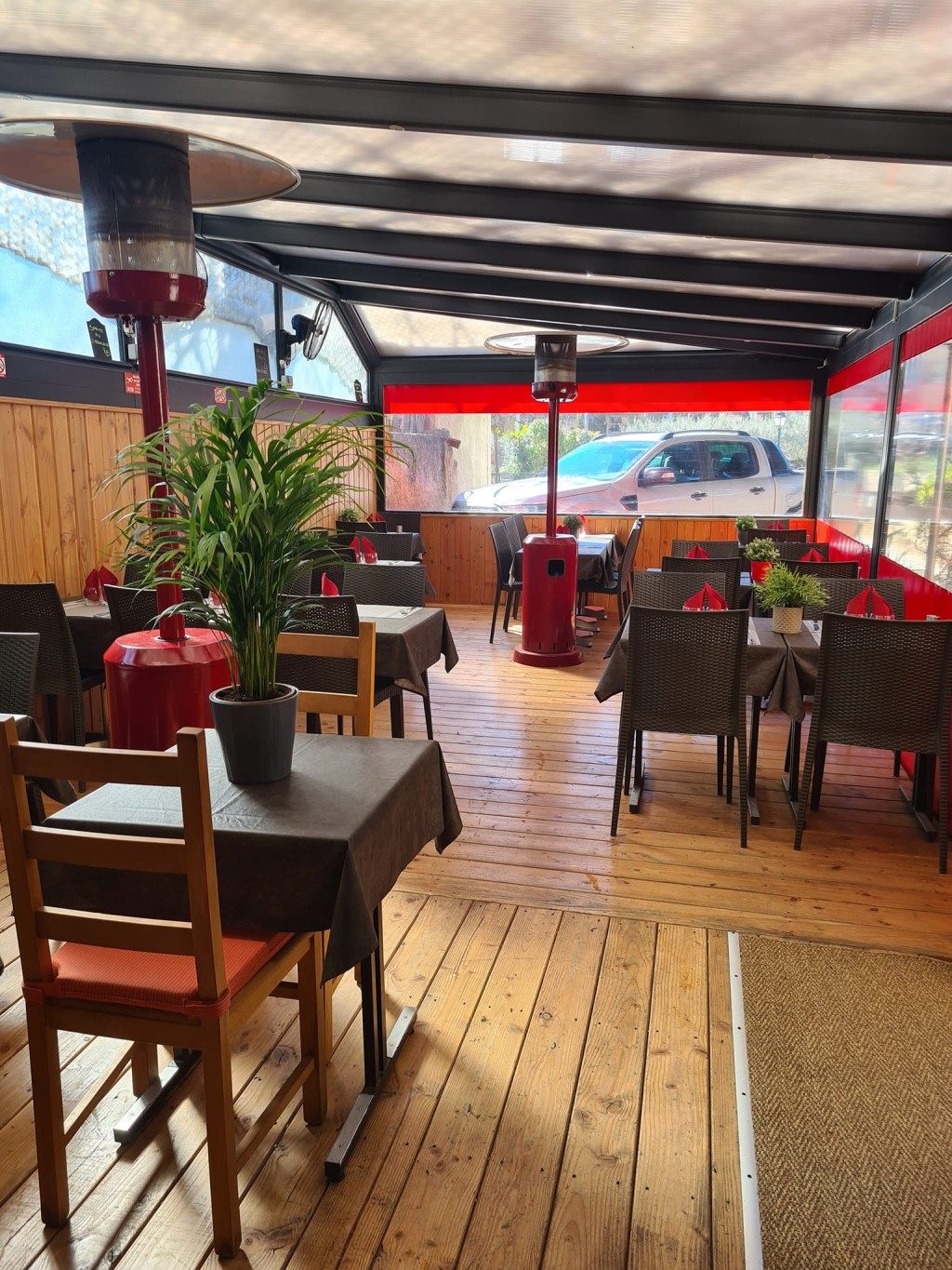 La terrasse couverte : plancher en bois, tables sombres, plantes vertes et chauffage d'extérieur